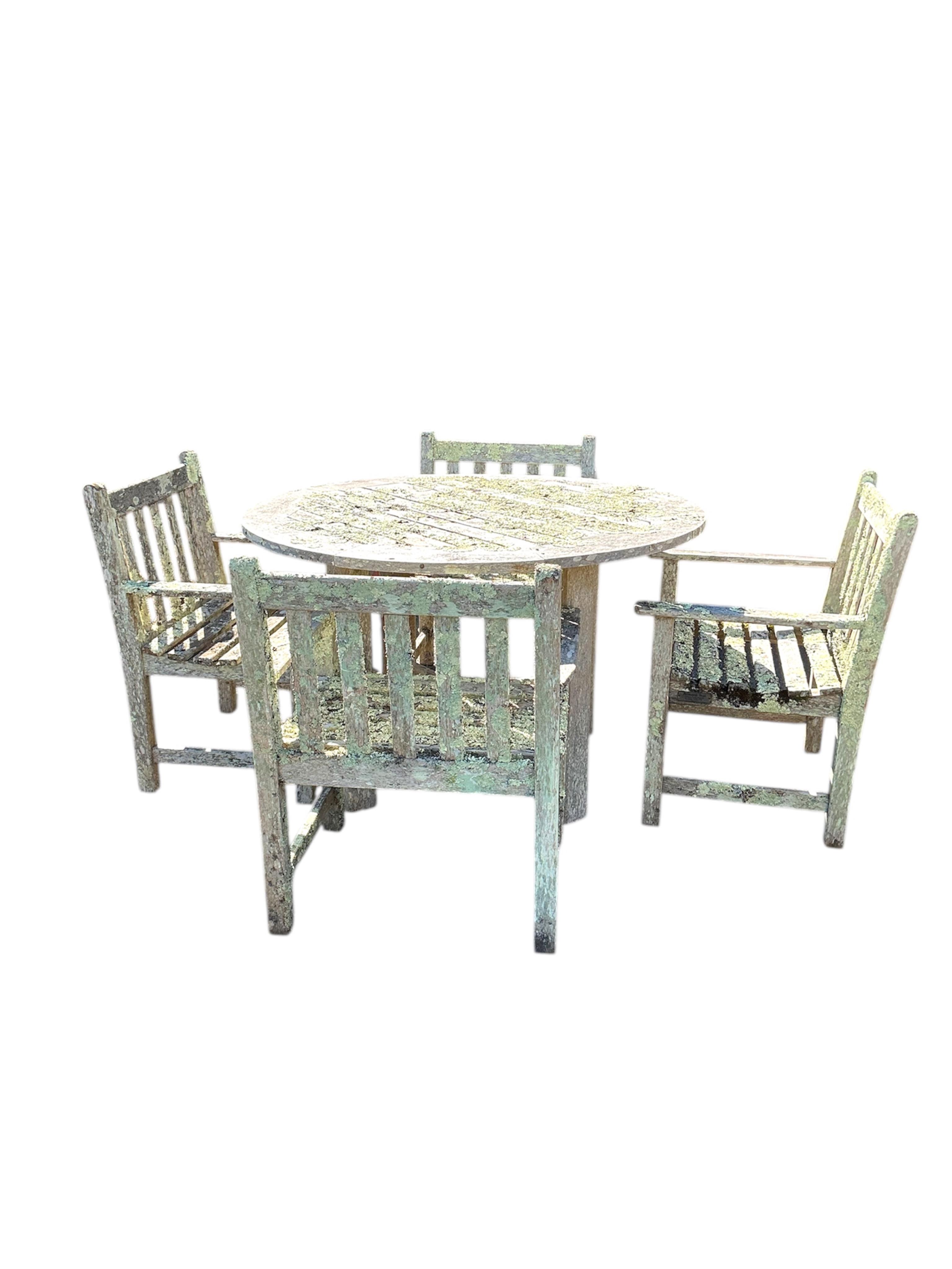 A weathered and lichen covered circular teak garden table, diameter 120cm, height 75cm and four armchairs